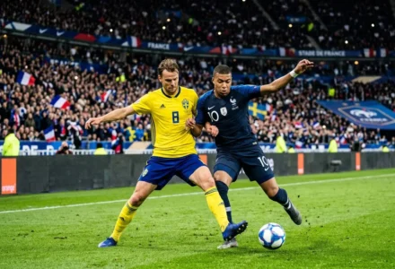 Deux joueurs en duel pour le ballon lors d’un match France-Suède, sous les tribunes pleines et drapeaux visibles. france suede foot