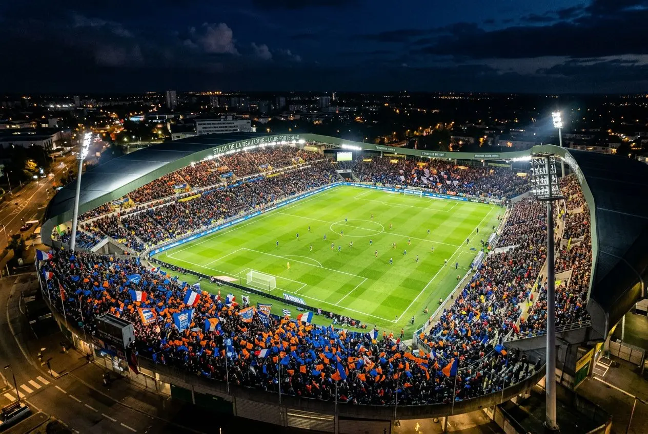 Stade de football nocturne rempli de spectateurs en tribunes orange et bleu, vue aérienne du match France Côte d’Ivoire à Nantes.