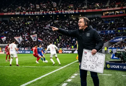 Entraîneur sur le bord du terrain, indiquant du doigt vers le jeu, tenant un tableau tactique lors d’un match de football. Stratégie footballistique au cœur de la séance.