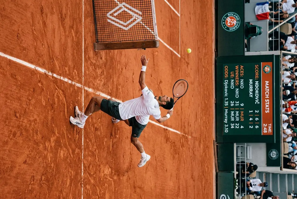 Joueur de tennis sur terre battue effectuant un smash près du filet lors d’un match, tableau des statistiques et spectateurs en arrière-plan. intégrer: comment gagner au tennis paris sportif