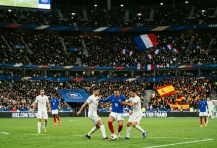 Match de football franco-espagnol avec joueurs en action: un joueur bleu contrôle le ballon entouré de défenseurs blancs dans un grand stade.