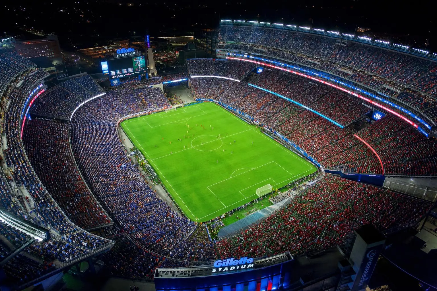 Stade bondé lors d’un match de football nocturne, vue aérienne du terrain vert entouré de tribunes remplies, ambiance intense pour une rencontre France-Maroc. analyse france maroc football