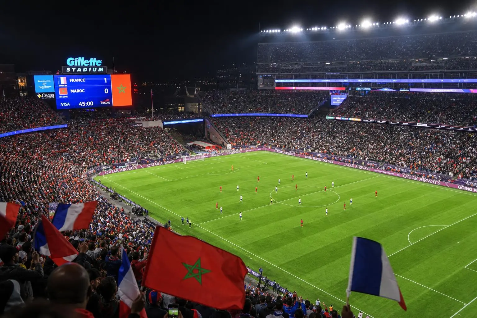 Stade de Gillette à nuit, ambiance festive avec drapeaux Maroc et France, match maroc-france en cours sur grand écran affichant score et temps.