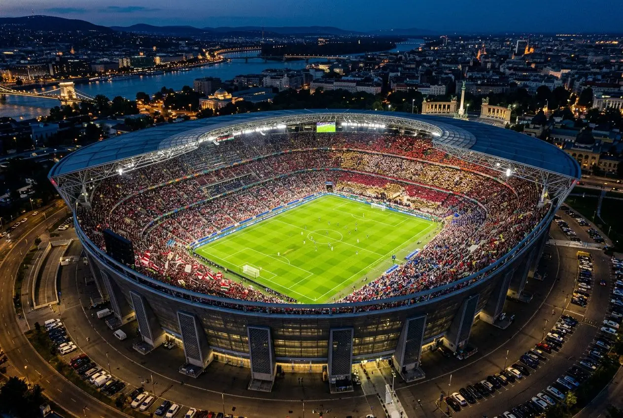 Stade illuminé vu du ciel lors d’un match, tribunes pleines et vue panoramique sur la ville nocturne. champions league format intégré.