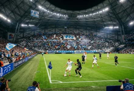 Stade plein lors d’un match de football européen, tribunes pleines de supporters bleus et blancs, action près de la ligne de touche et drapeau MARSEILLE en avant-plan. résultat tours préliminaires champions league est évoqué par le contexte.