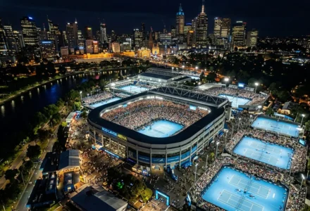 Vue aérienne nocturne de l’Open d’Australie à Melbourne avec le stade principal et des terrains extérieurs, éclairés et entourés par la ville, favoris pour l’open d'Australie.