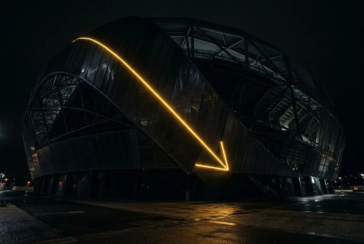 Stade moderne éclairé nocturne avec bande lumineuse diagonale orange, façade métallique et cône de lumière au sol. Intègre le concept d’équipes relégables ligue 1.