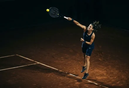 Joueur de tennis en action sur terre battue, effectuant un coup droit en plein saut, avec balle en vol. comment gagner au tennis paris sportif intégré naturellement.